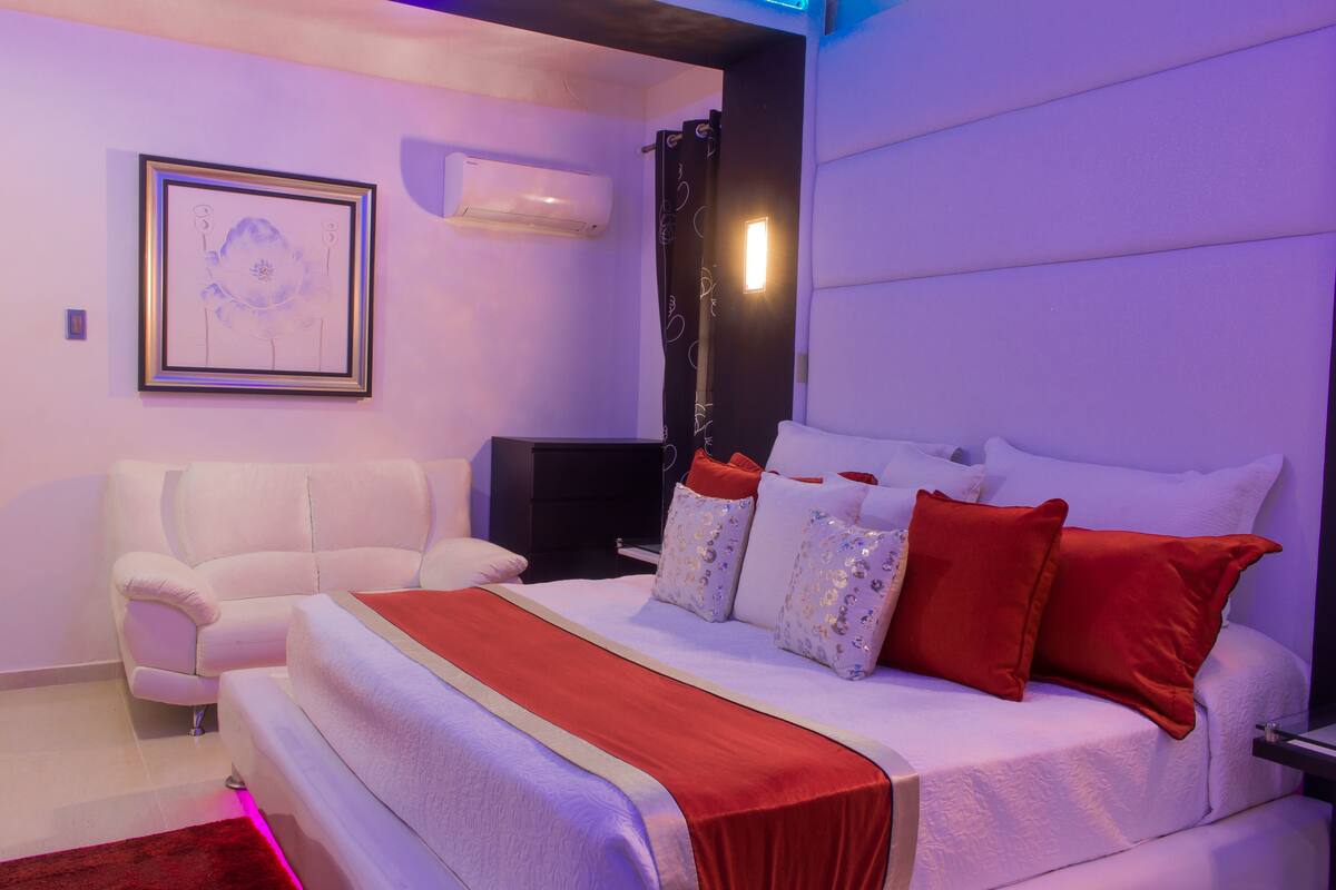 Une chambre moderne avec un grand lit, un canapé blanc et un téléviseur à écran plat.