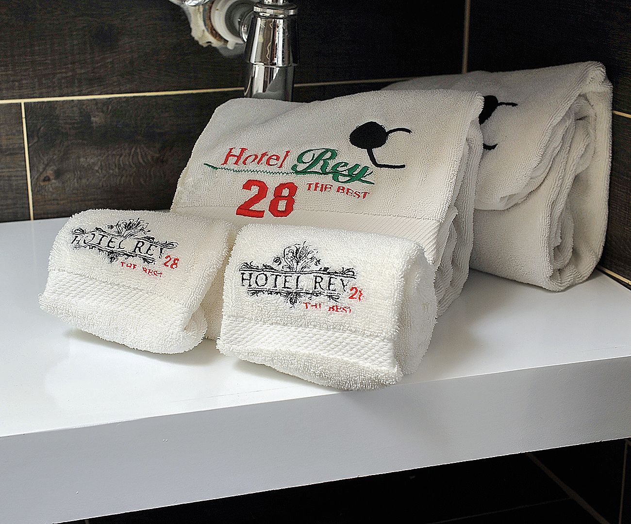 A bathroom with a white sink, two towels with 'Hotel Rey' and '28' embroidered on them, and a silver faucet.