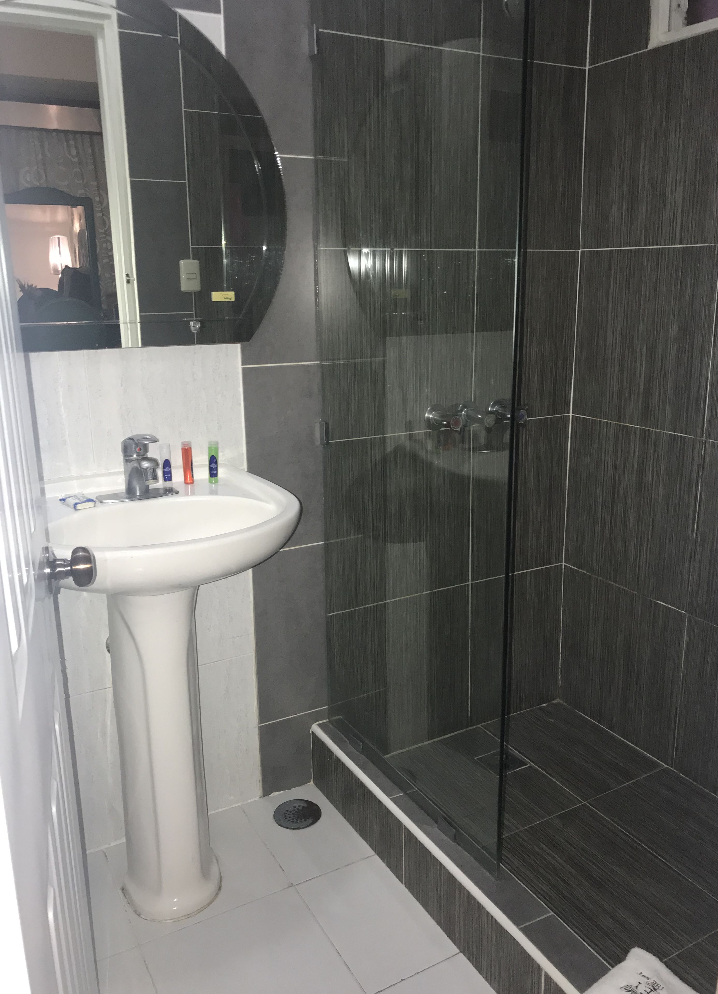 Une salle de bain avec un lavabo sur colonne blanc, un miroir et une cabine de douche en verre.