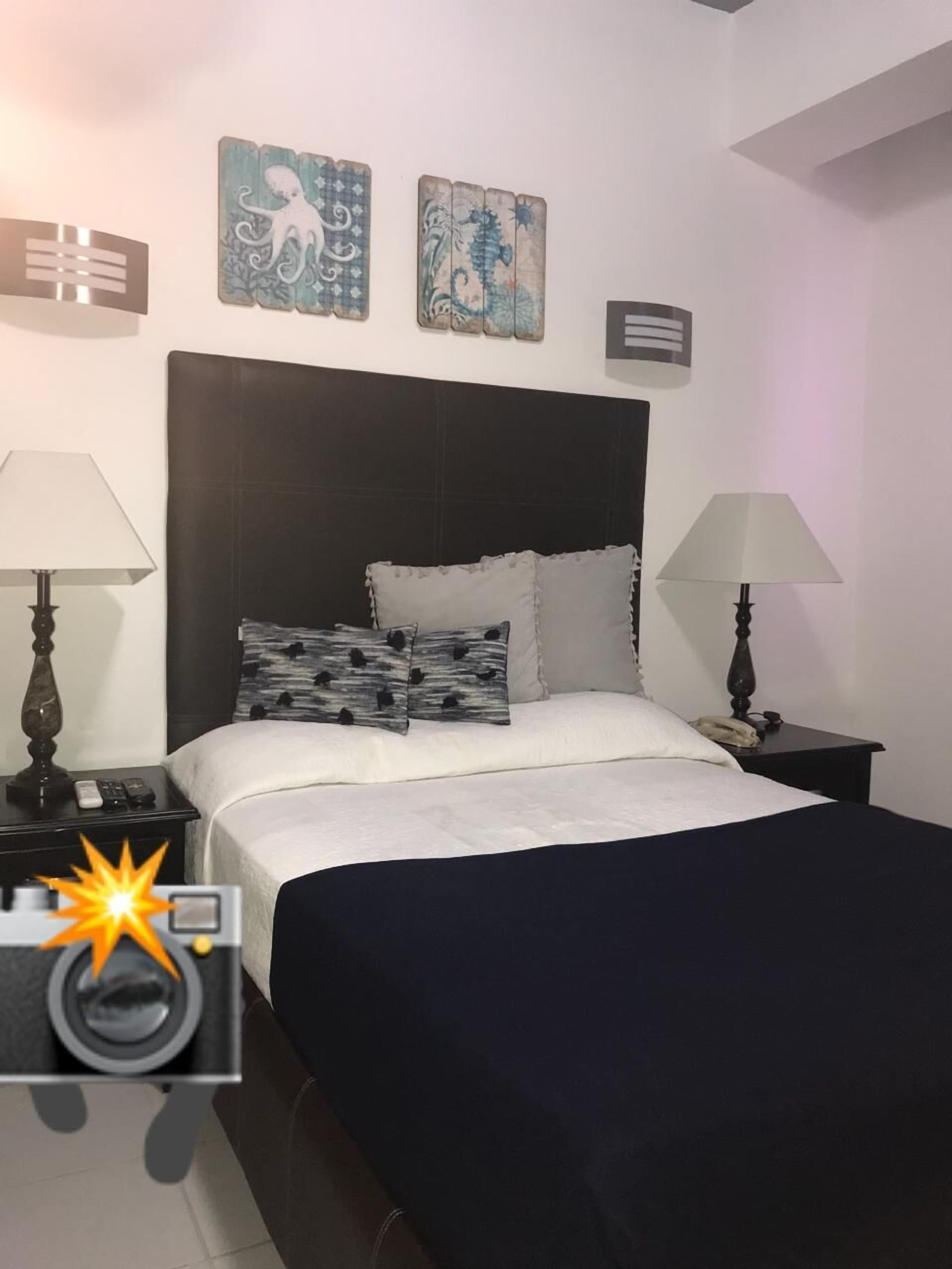 Un dormitori amb un llit, dues taules de nit, una petita taula auxiliar, un capçal i decoració a la paret.