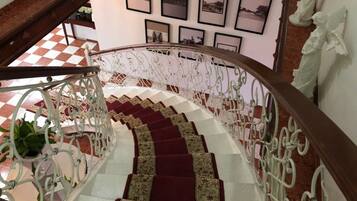 A spiral staircase with a red carpet and white railing, leading to a room with a checkered floor and framed pictures on the wall.