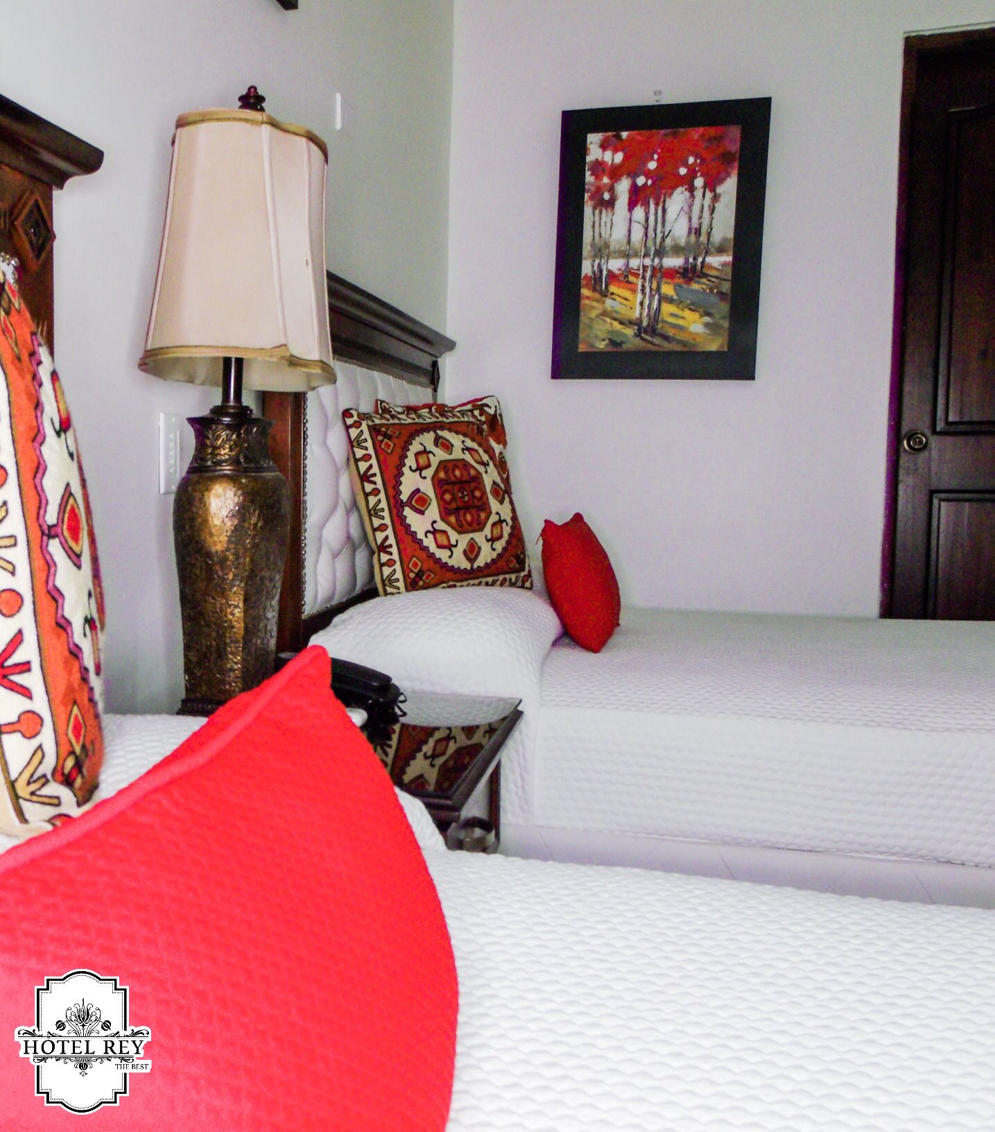 Una habitación de hotel con dos camas, una lámpara, un cuadro y una puerta.