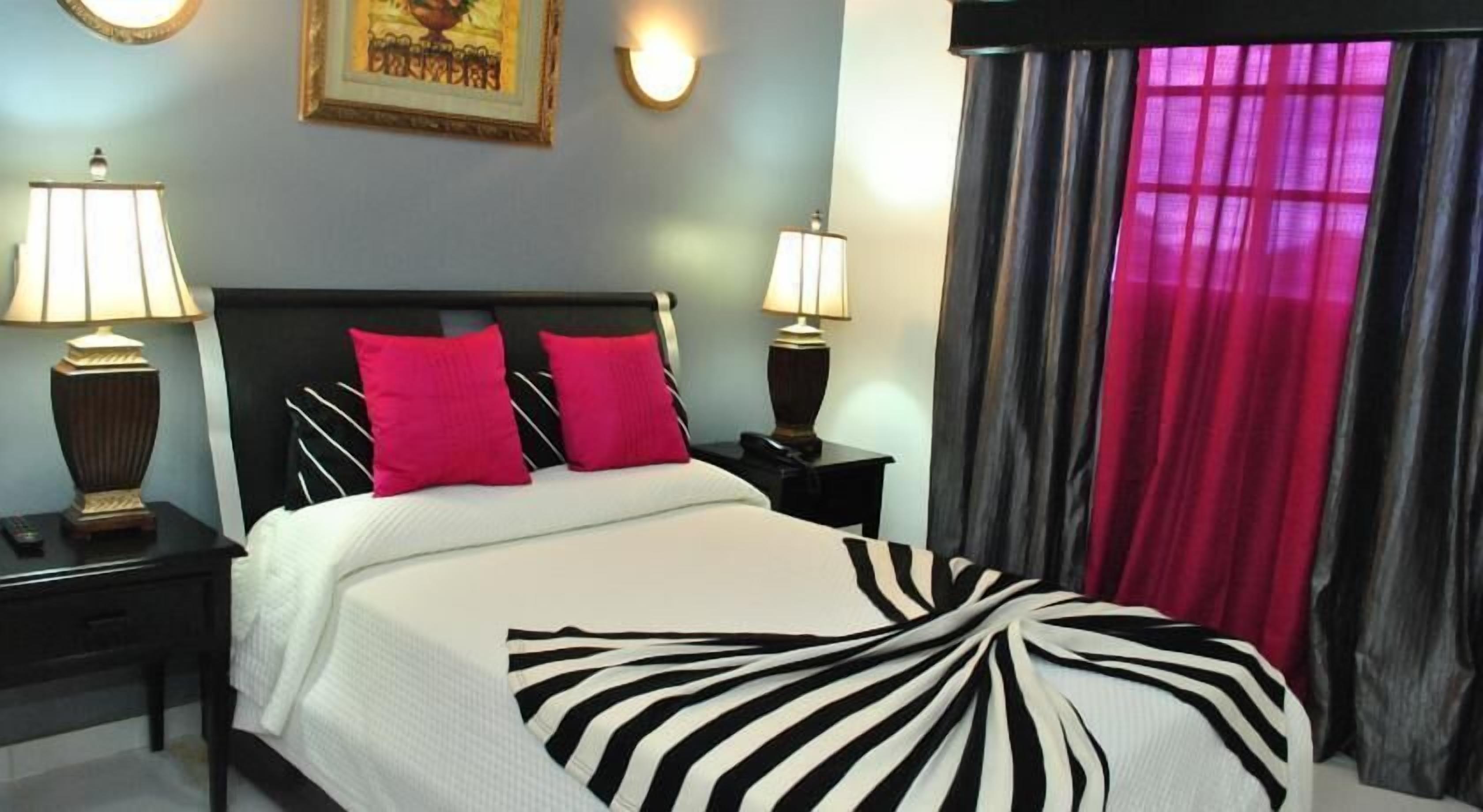 Una camera d'albergo con un letto, due comodini, due lampade, un quadro appeso alla parete e una finestra con tende.
