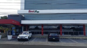 Hotel anomenat "Hotel Rey" amb façana moderna, dos cotxes aparcats al davant i un tendal vermell.