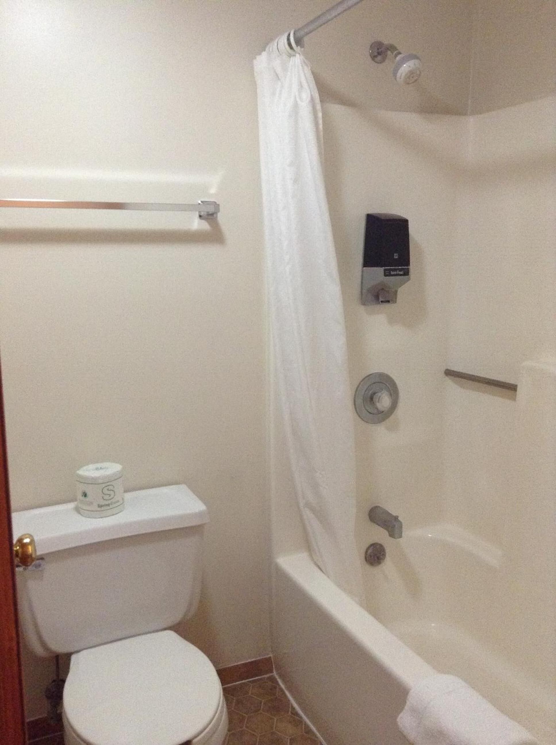 A bathroom with a toilet, a shower with a glass door, and a soap dispenser on the wall.