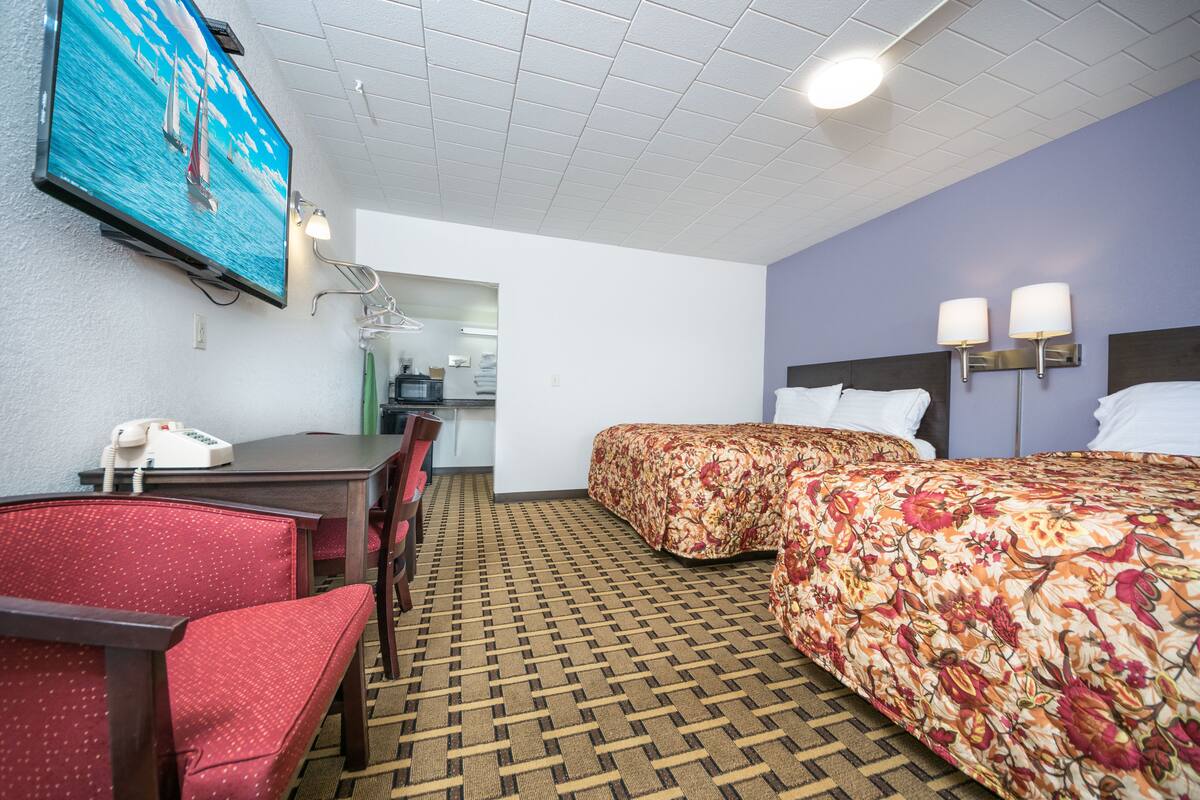 A hotel room with two beds, a desk with a telephone, a TV mounted on the wall, and a patterned carpet.