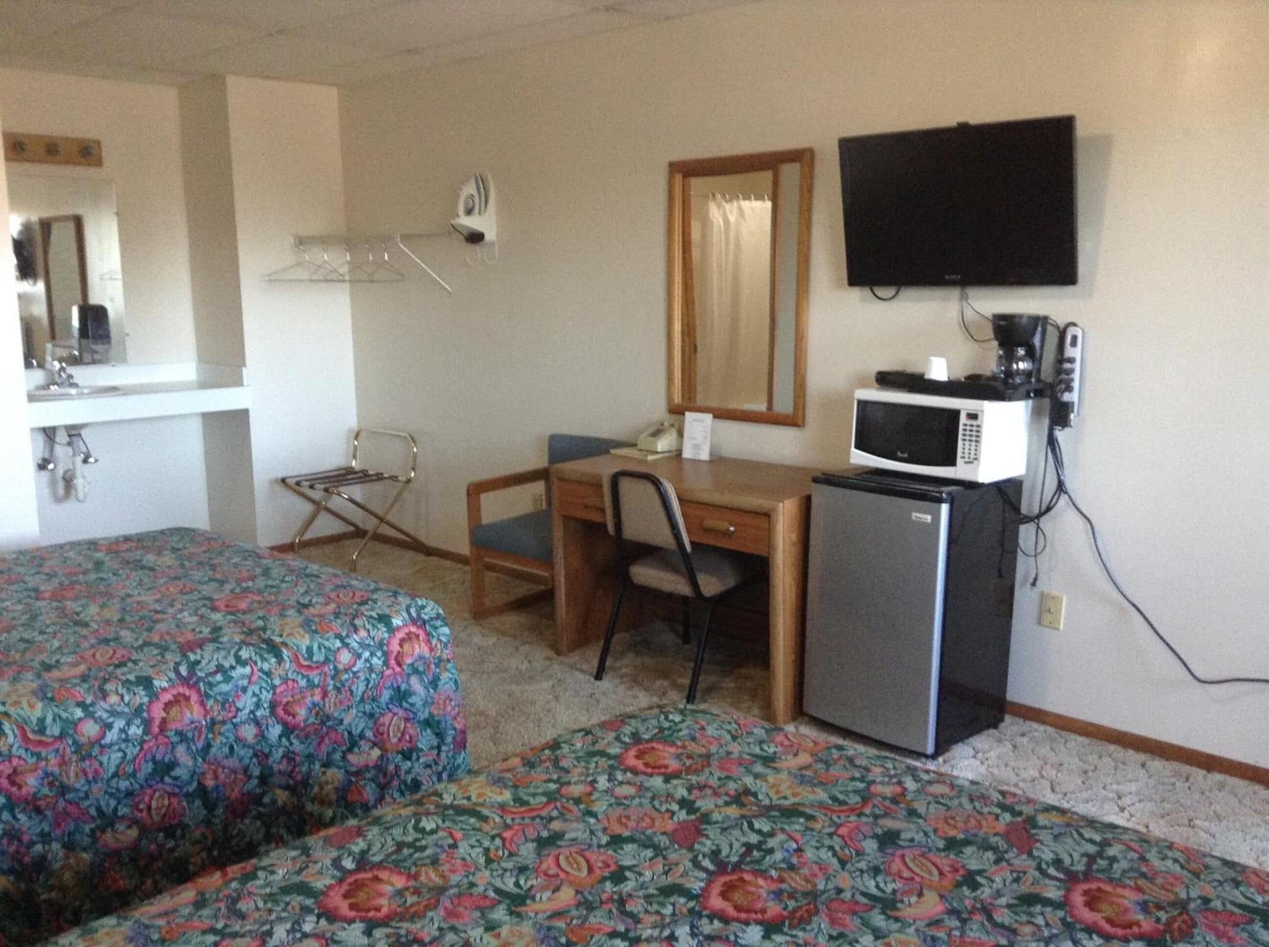 Une chambre d’hôtel avec deux lits, un bureau, une chaise, un four à micro-ondes et un téléviseur.