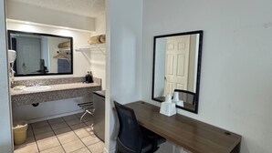 A hotel room with a wooden desk, a black office chair, a large mirror, a tiled floor, and a small kitchenette area. - National Inn Garden Grove (Garden Grove)