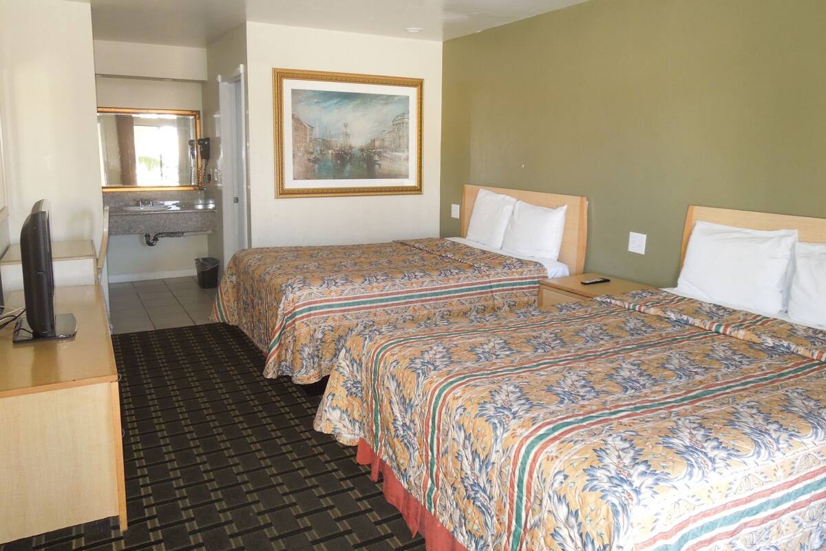 A hotel room with two beds, a desk with a computer, a mirror, and a painting on the wall.