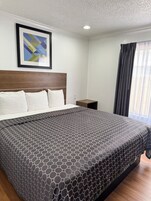 Habitación de hotel con una cama grande, cabecera, mesita de noche, un cuadro enmarcado en la pared y una ventana con cortinas.