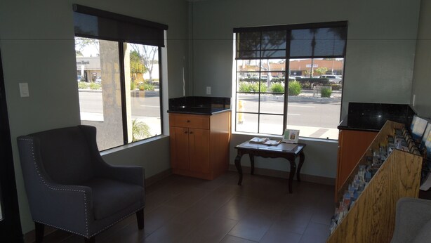 A room with a grey armchair, a small wooden table, and a kitchen counter with a black appliance. - National Inn Garden Grove (Garden Grove)