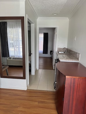 A room with a wooden floor, a kitchen area with a sink and countertop, and a hallway leading to another room. - National Inn Garden Grove (Garden Grove)