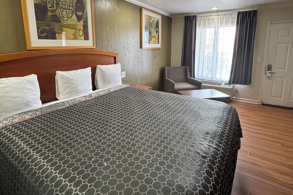 A hotel room with a large bed, a chair, a table, and two framed artworks on the wall.