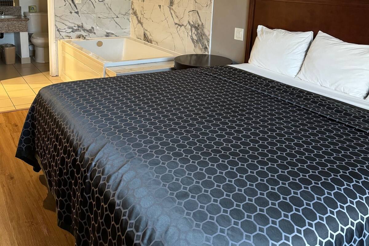 A hotel room with a large bed, a bathroom with a marble wall, and a framed picture on the wall.