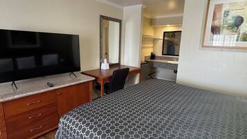 A hotel room with a bed, a desk, a television, a mirror, and a painting on the wall.