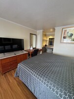A hotel room with a bed, a desk, a television, a mirror, and a painting on the wall.