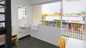 A hotel room with a bunk bed, a sink, a mirror, a window with a view of the city, and a table with a chair. - Palm Beach Hotel (Palm Beach)