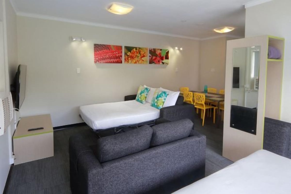 A hotel room with a bed, a sofa, a dining table with chairs, and a mirror.