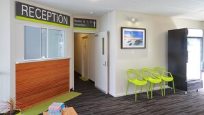 A reception area with a sign indicating rooms and amenities, a reception desk, a framed picture on the wall, and three bright green chairs. - Palm Beach Hotel (Palm Beach)