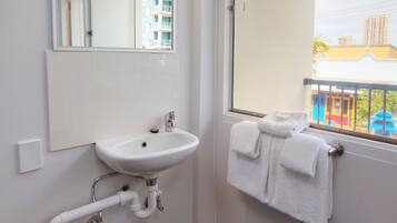 Un baño con un lavabo blanco, un espejo y una ventana con vistas a edificios.