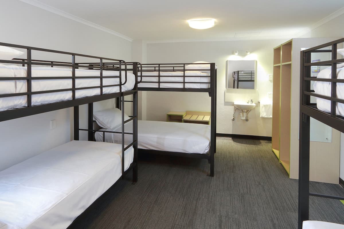 Un dormitorio con literas, tres literas, un baño pequeño con lavamanos y espejo, y piso alfombrado.