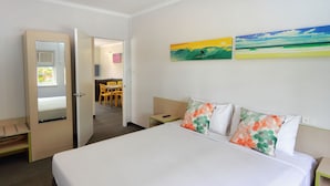 A hotel room with a bed, a desk, a chair, and a small table. There is a door leading to a bathroom and a hallway. - Palm Beach Hotel (Palm Beach)