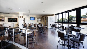 A spacious restaurant with high ceilings, multiple tables and chairs, and large windows offering a view of the outside. - Palm Beach Hotel (Palm Beach)