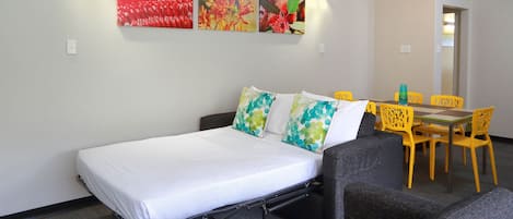 A room with a bed, a sofa, a dining table with chairs, and wall art.