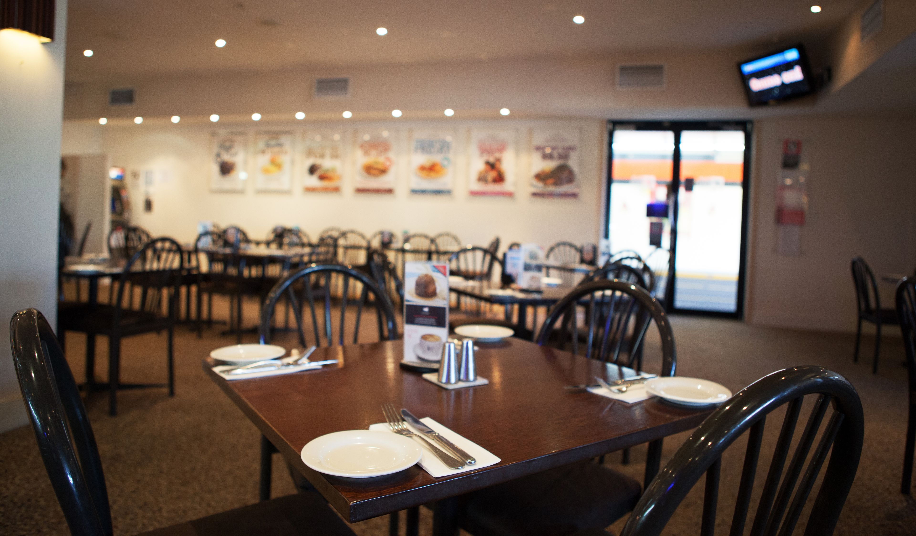 Un espace repas avec des tables préparées pour deux personnes, des chaises et un présentoir à menus.