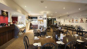 A restaurant with multiple dining tables and chairs, a counter with a menu, and various posters on the walls.