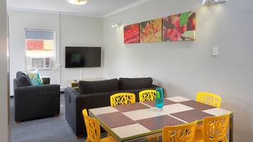 Ein modernes Wohnzimmer mit einer Sofagarnitur, einem Esstisch mit gelben Stühlen und einem flachbildfernseher an der Wand.