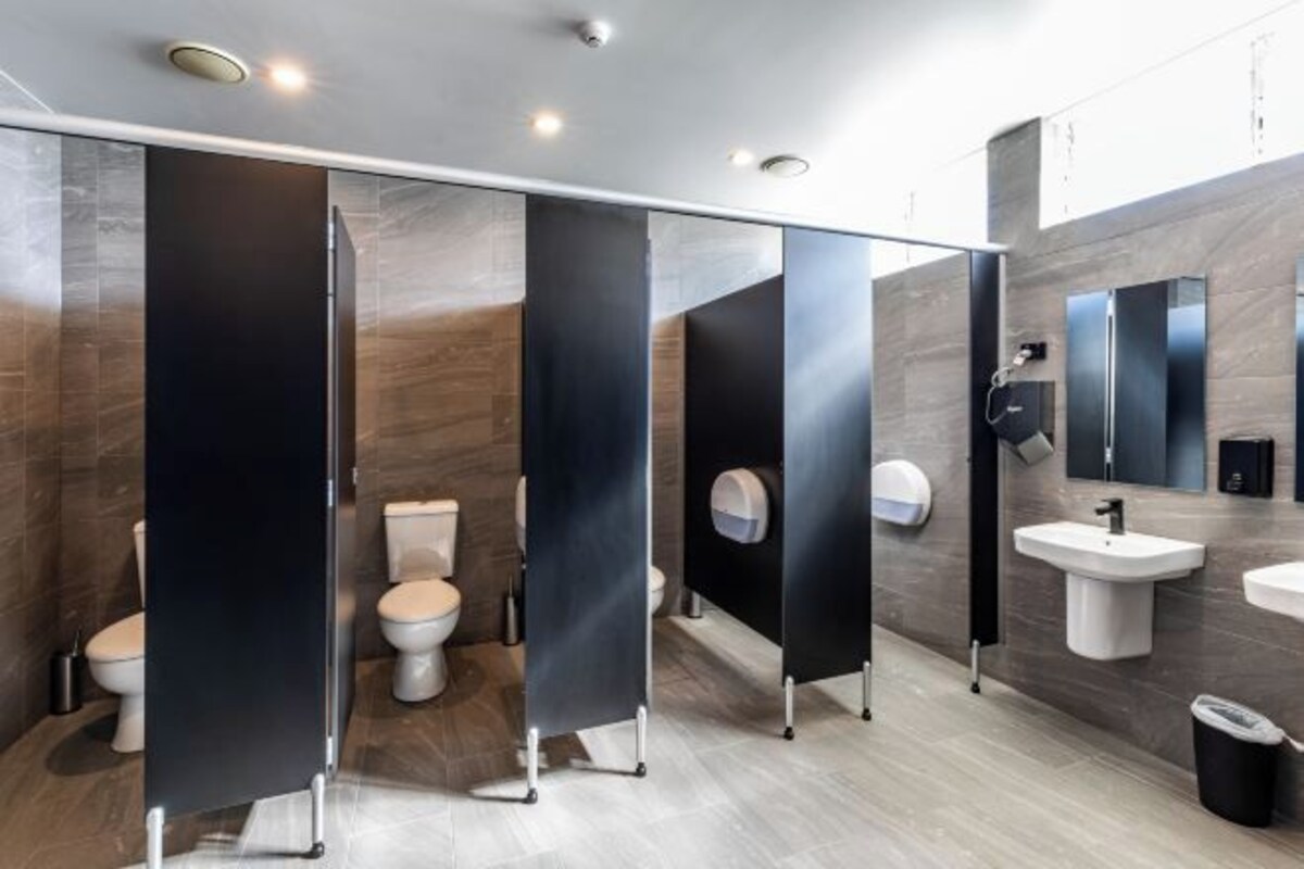 A modern bathroom with three toilets, a sink, and a mirror.