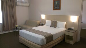 Habitación de hotel con una cama grande, una mesita de noche, una silla, una pequeña mesa con un florero y un aire acondicionado instalado en la pared.