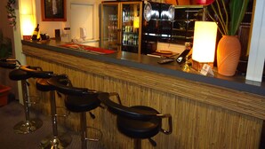 Un espace bar avec des tabourets, un comptoir et un grand vase rempli de fleurs rouges.