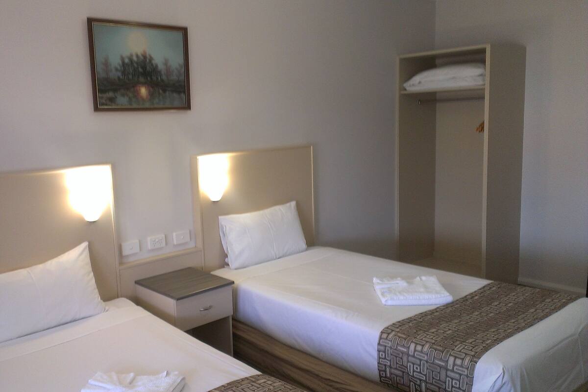 A hotel room with two beds, a nightstand, a painting on the wall, and a wardrobe.