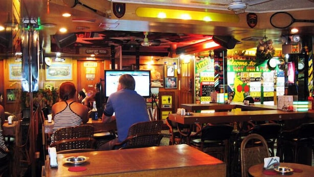 A restaurant with wooden tables and chairs, a TV screen, and various signs and decorations on the walls. - Slouch Hat Hotel (Manila)
