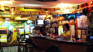 A bar with a neon sign, a bartender, and various bottles and glasses on shelves. - Slouch Hat Hotel (Manila)