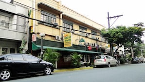 A building with a green awning, a sign for a bar and restaurant, and parked cars on the street. - Slouch Hat Hotel (Manila)