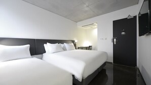 Una habitación de hotel moderna con dos camas, una puerta oscura y un televisor de pantalla plana montado en la pared.