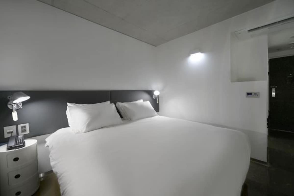 Une chambre d’hôtel moderne avec un grand lit, des lampes de chevet, une table de nuit et un panneau de commande au mur.