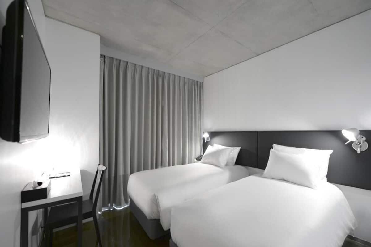 Une chambre d’hôtel avec deux lits, un bureau, une chaise, une télévision et un rideau.