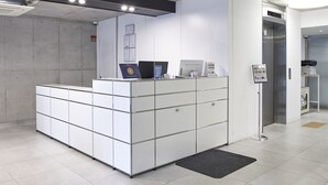 Una mesa de recepción con computadora, impresora y una pequeña zona de espera.