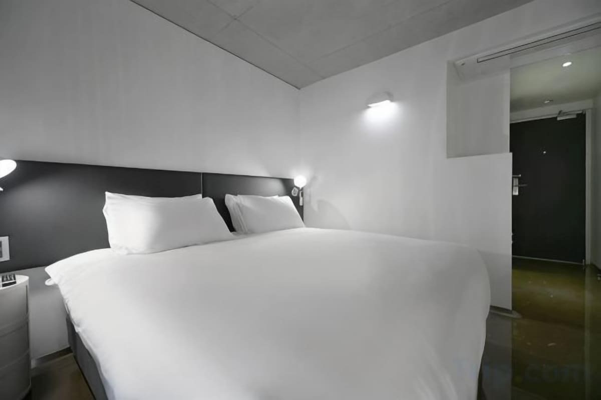 Una habitación de hotel moderna con una cama grande, mesitas de noche y un velador.
