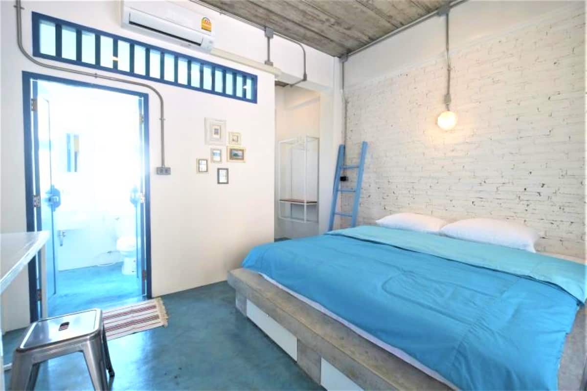A bedroom with a bed, a ladder, a stool, and a door leading to a bathroom.