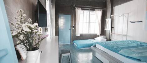 Un dormitorio moderno con una cama, una mesita de noche y un taburete pequeño. Hay una ventana con cortinas, una puerta y un televisor montado en la pared.