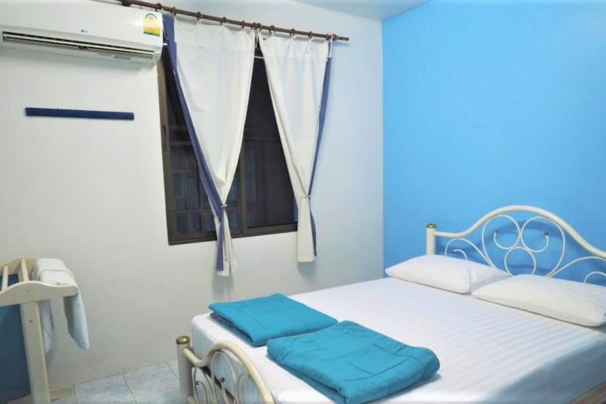 A bedroom with a bed, a window with curtains, an air conditioning unit, and a bedside table.