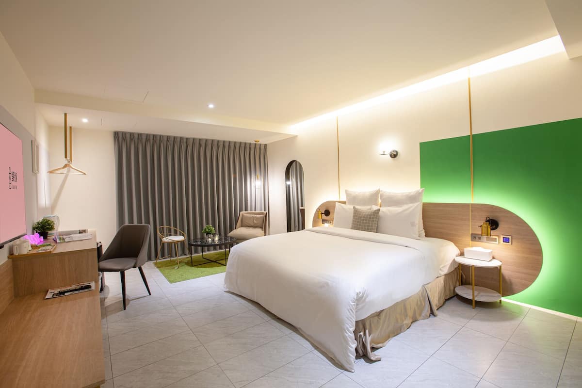 Une chambre d’hôtel moderne avec un grand lit, un bureau, une chaise, une petite table et un mur d’accent vert.