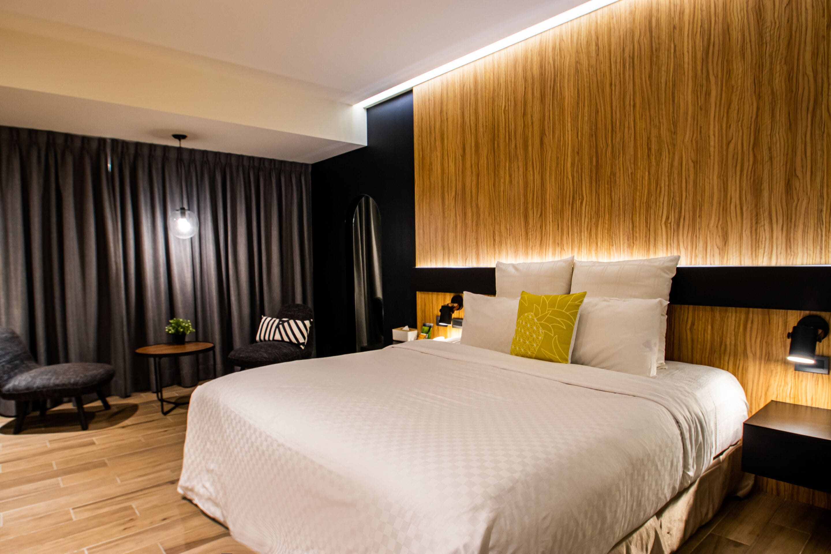 Una habitación de hotel moderna con una cama grande, un pequeño rincón de descanso y una mesita de noche con lámpara.