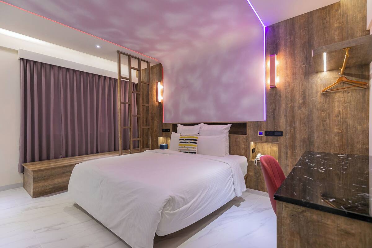 Une chambre à coucher moderne avec un grand lit, un lambris en bois, un banc en bois, une chaise rouge et un plan de travail noir.