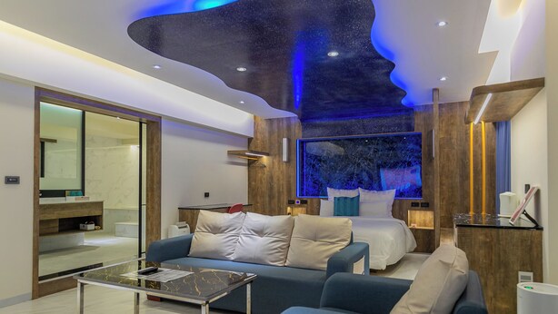 A modern hotel room with a large bed, a sofa, a glass coffee table, and a large mirror. - Lilai Travel - Lilia Motel (Taoyuan City)